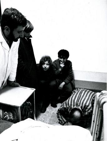 tre giovani spettatori sulle panche a loro disposizione in una delle due stanze corsie, a destra il performer infermiere controlla l'internato