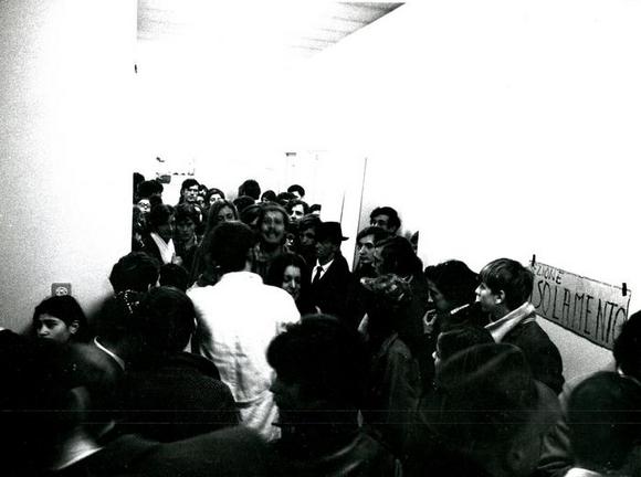 Tra il pubblico assiepato nel corridoio che conduce allo spazio di isolamento si nota il camice bianco del performer nella parte dell'infermiere